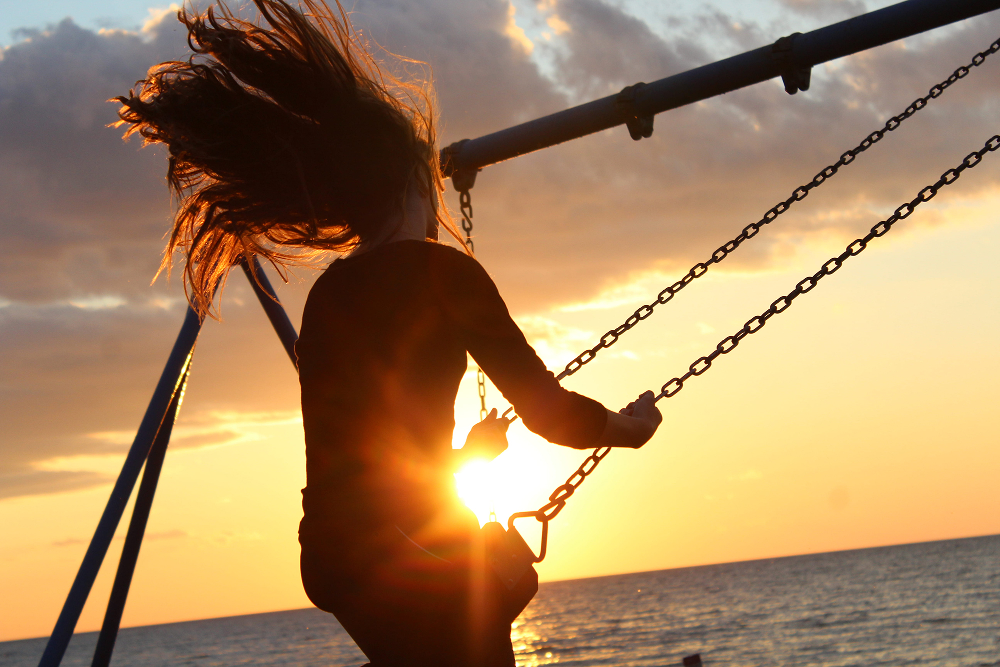 woman swinging near ocean at sunset